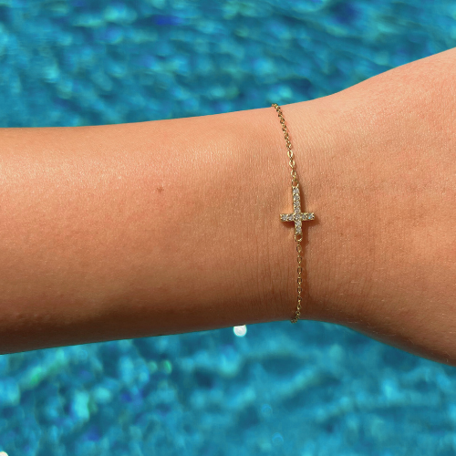 A gold cross bracelet with cubic zirconia with an adjustable chain link.