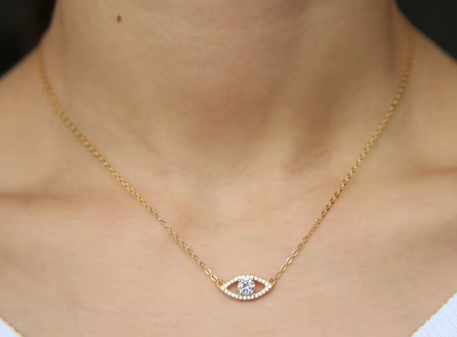 A gold necklace with a cubic zirconia evil eye pendant, featuring a curved design with multiple smaller cubic zirconia stones around the eye.